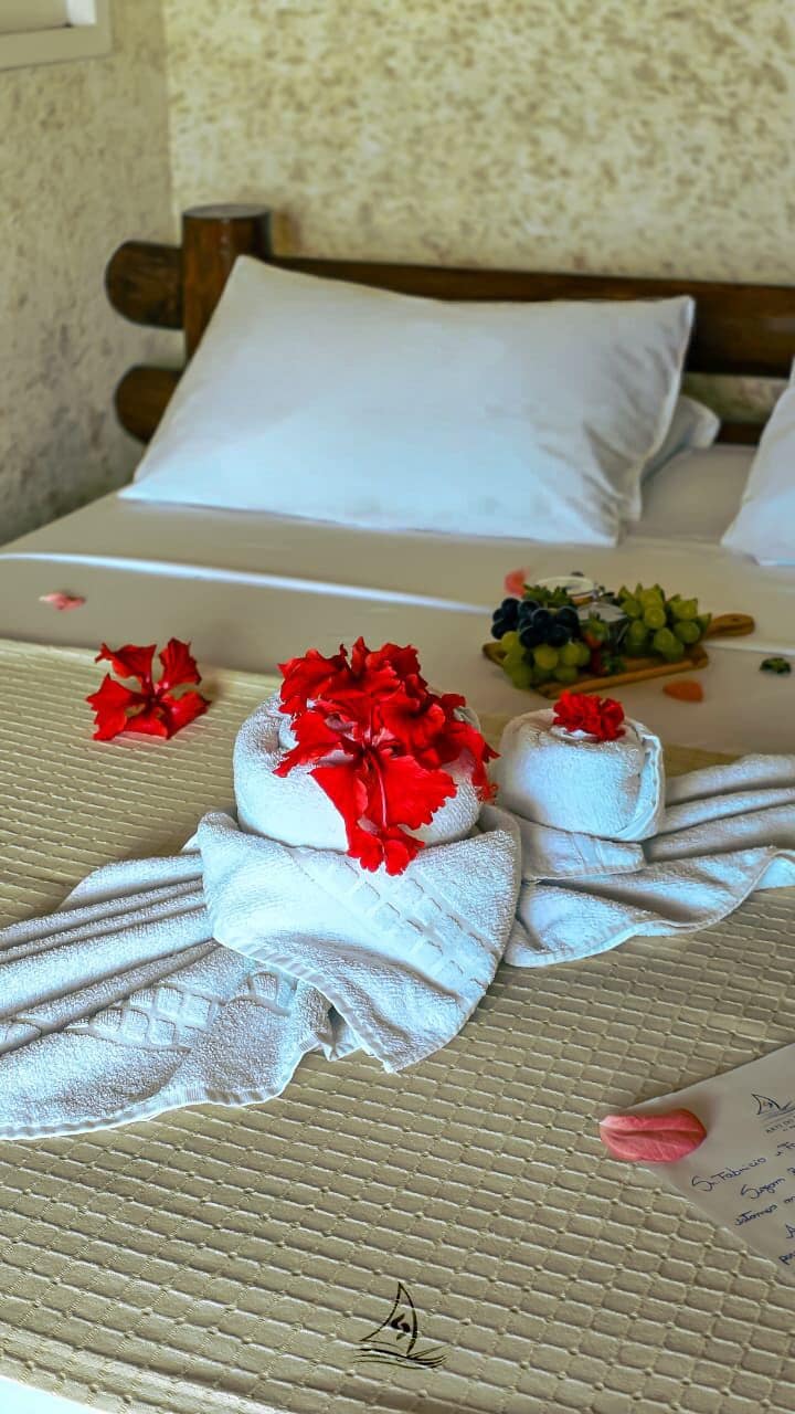 A neatly made bed with towels and flowers, a wooden headboard, and a wall with a textured pattern.