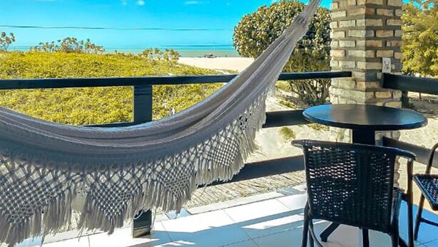 Eine Hängematte unter einem Reetdach, ein Tisch und Stühle auf einer Terrasse mit Blick auf das Meer.
