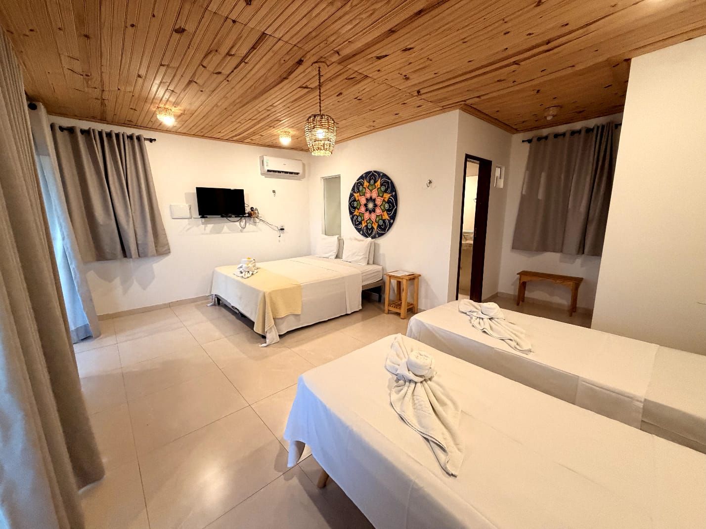 A hotel room with two beds, a television, a decorative wall piece, and a wooden ceiling.