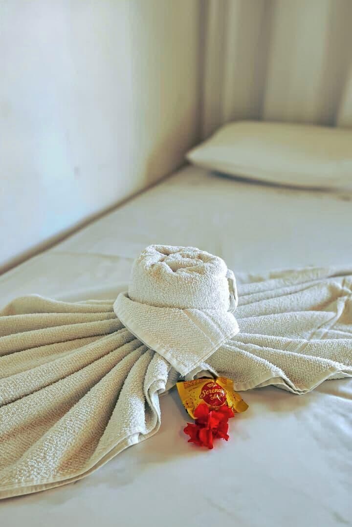 Un letto rifatto con cura, un asciugamano piegato e un piccolo regalo sul cuscino.