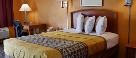 A hotel room with a large bed, two bedside lamps, a desk with a chair, a telephone, and a framed picture on the wall.