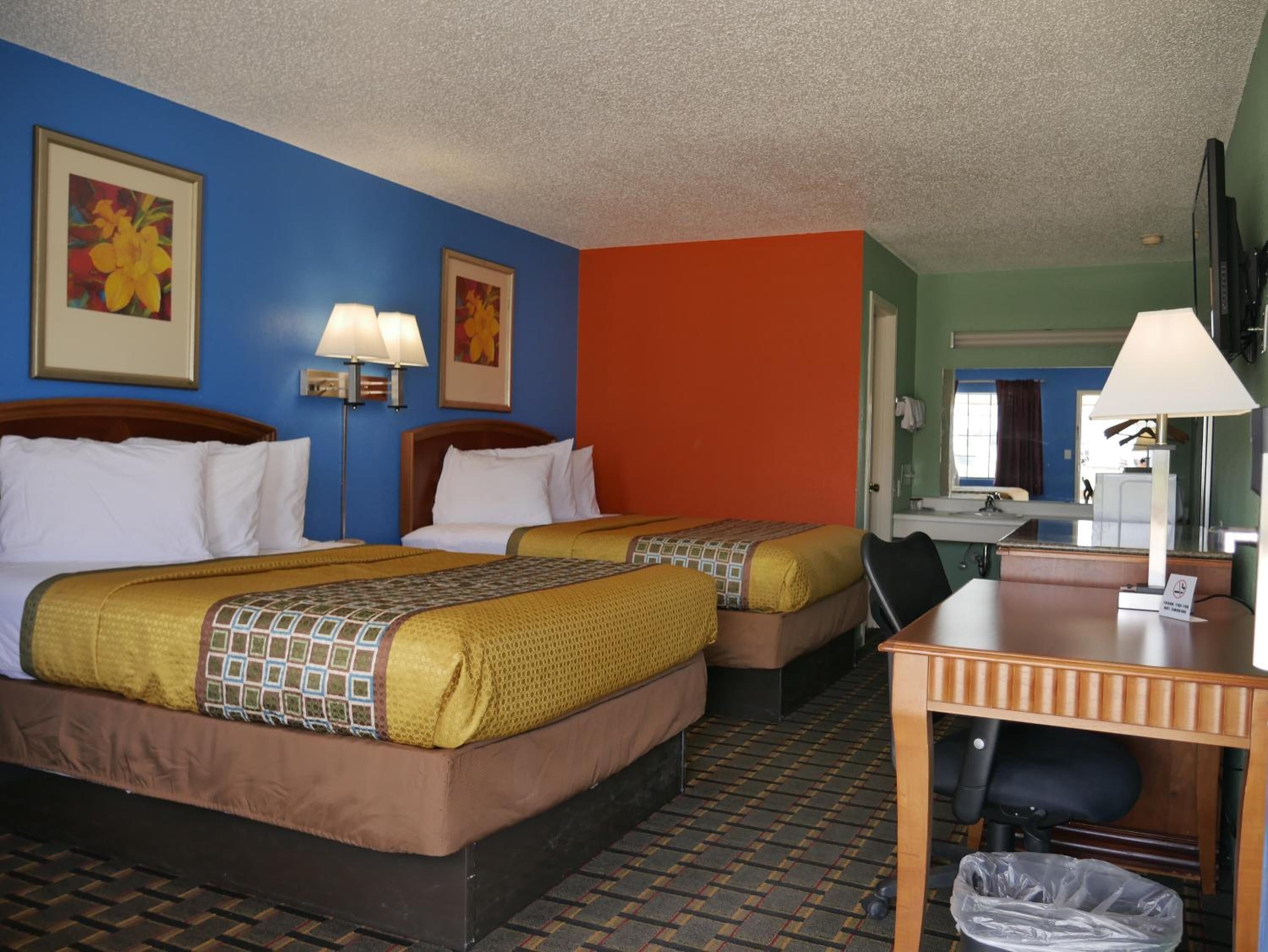 A hotel room with two beds, a desk, and a bathroom visible in the background.