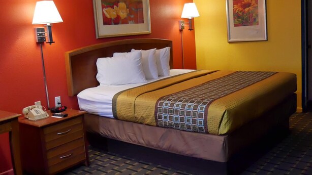 A hotel room with a bed, bedside lamps, a telephone, and a clock on the nightstand. - Morning Star Inn (Anson)