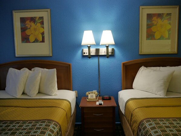 Una habitación de hotel con dos camas, una mesita de noche con teléfono y reloj, y lámparas fijadas a la pared.