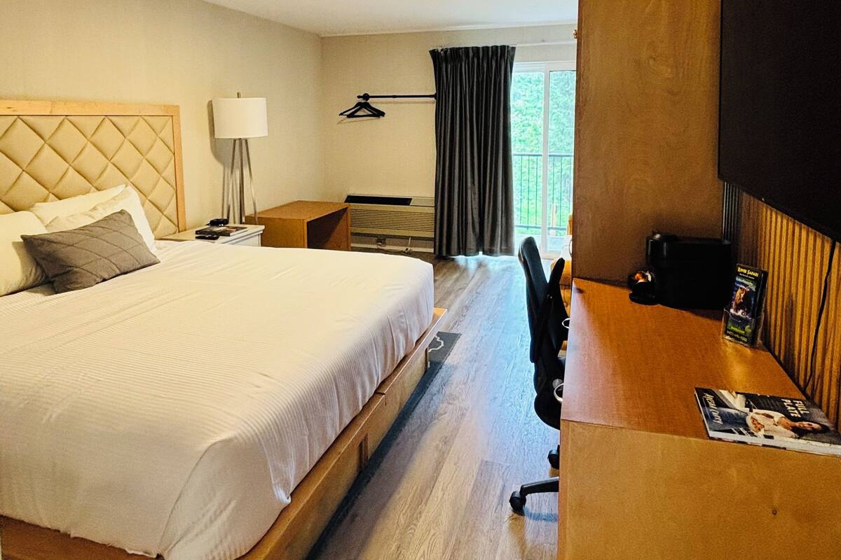 Ett hotellrum med en stor säng, ett skrivbord, en tv och ett fönster med gardiner.