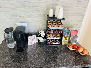 A kitchen counter with a coffee maker, a water dispenser, a card holder, a basket of apples, and a rack of Nespresso cups and pods. - Hotel Civilia Lakeside by Civilia Golf Retreat (Clearwater)