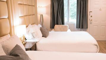 Une chambre d’hôtel avec deux lits, une tête de lit, une table de chevet avec une lampe et une fenêtre avec des rideaux.