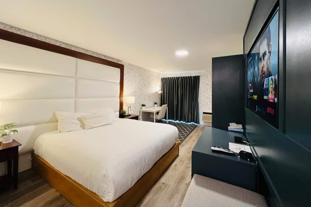 Ett modernt hotellrum med en stor säng, ett skrivbord, en TV och ett litet bord med en lampa.