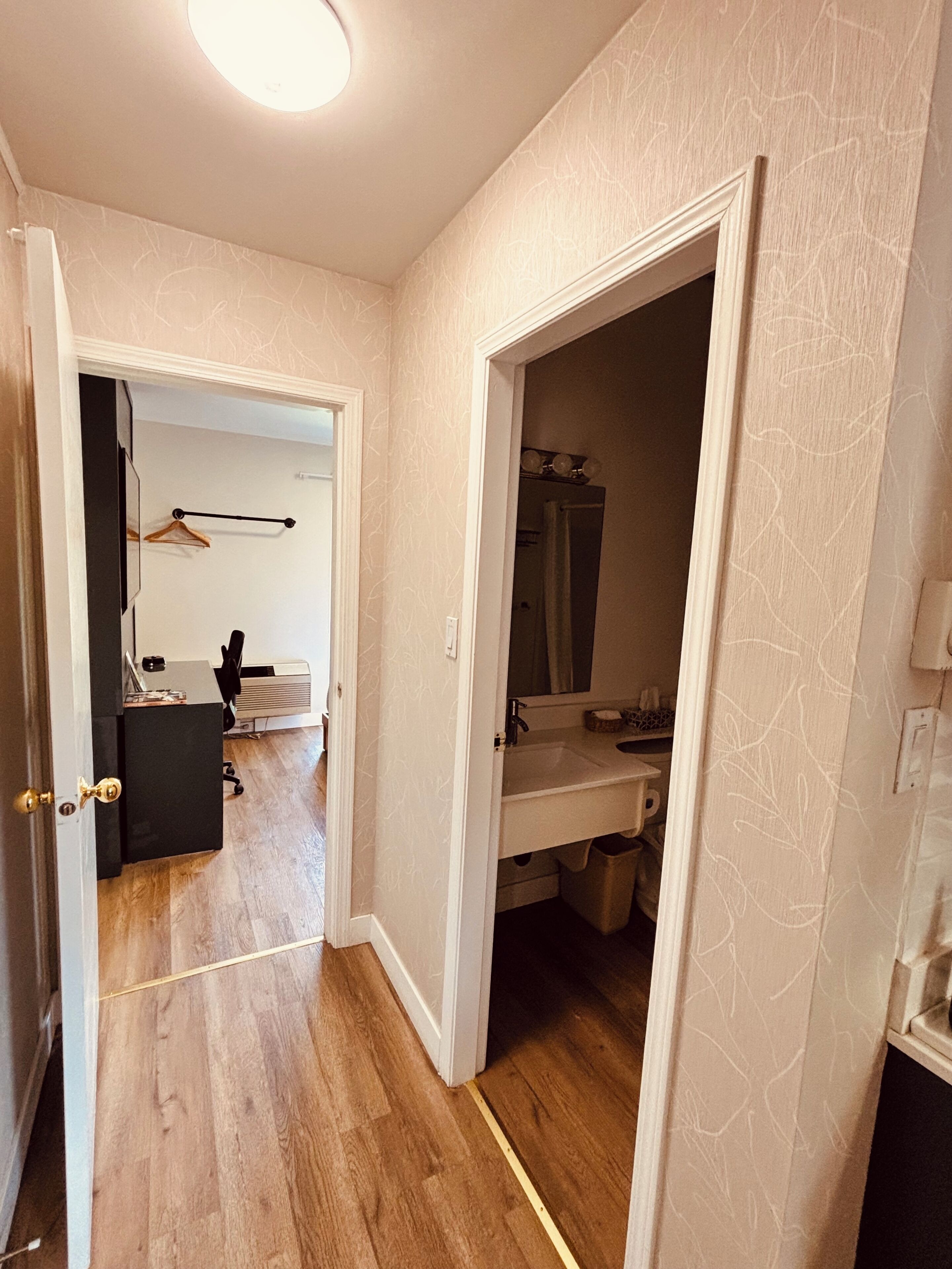 A hallway with a wooden floor, a black office chair, a desk, and a hanging coat rack.