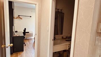A hallway with a wooden floor, a black office chair, a desk, and a hanging coat rack.