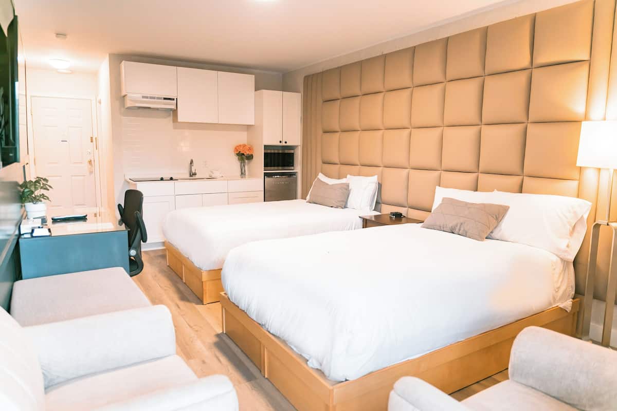 Ett modernt hotellrum med två sängar, ett litet kök och en sittgrupp.