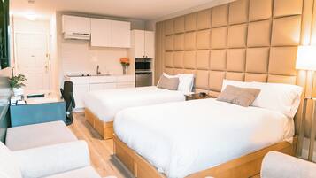 A modern hotel room with two beds, a kitchenette, and a seating area.