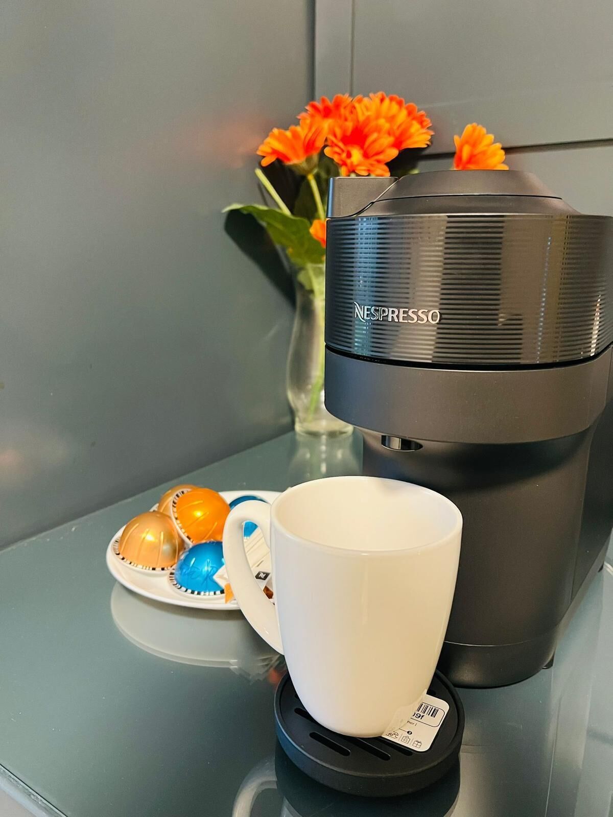 Una máquina de café Nespresso sobre una encimera con una taza blanca y un plato de cápsulas de café de colores.