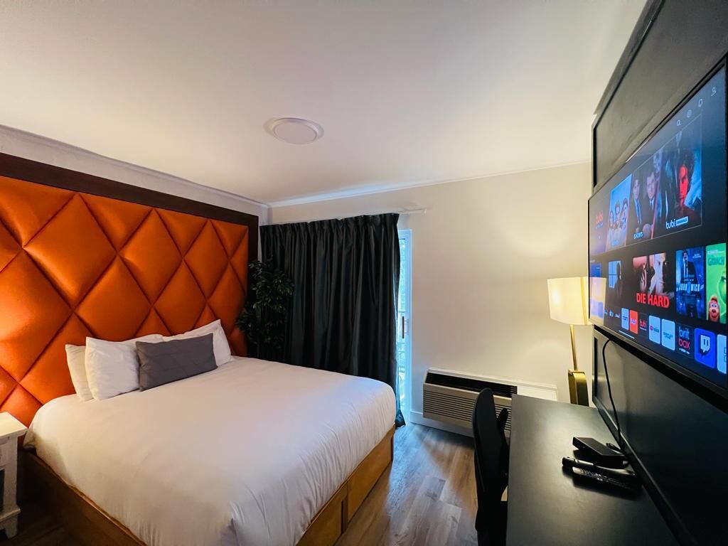 Habitación de hotel con una cama grande, un televisor en la pared y una ventana con cortinas.