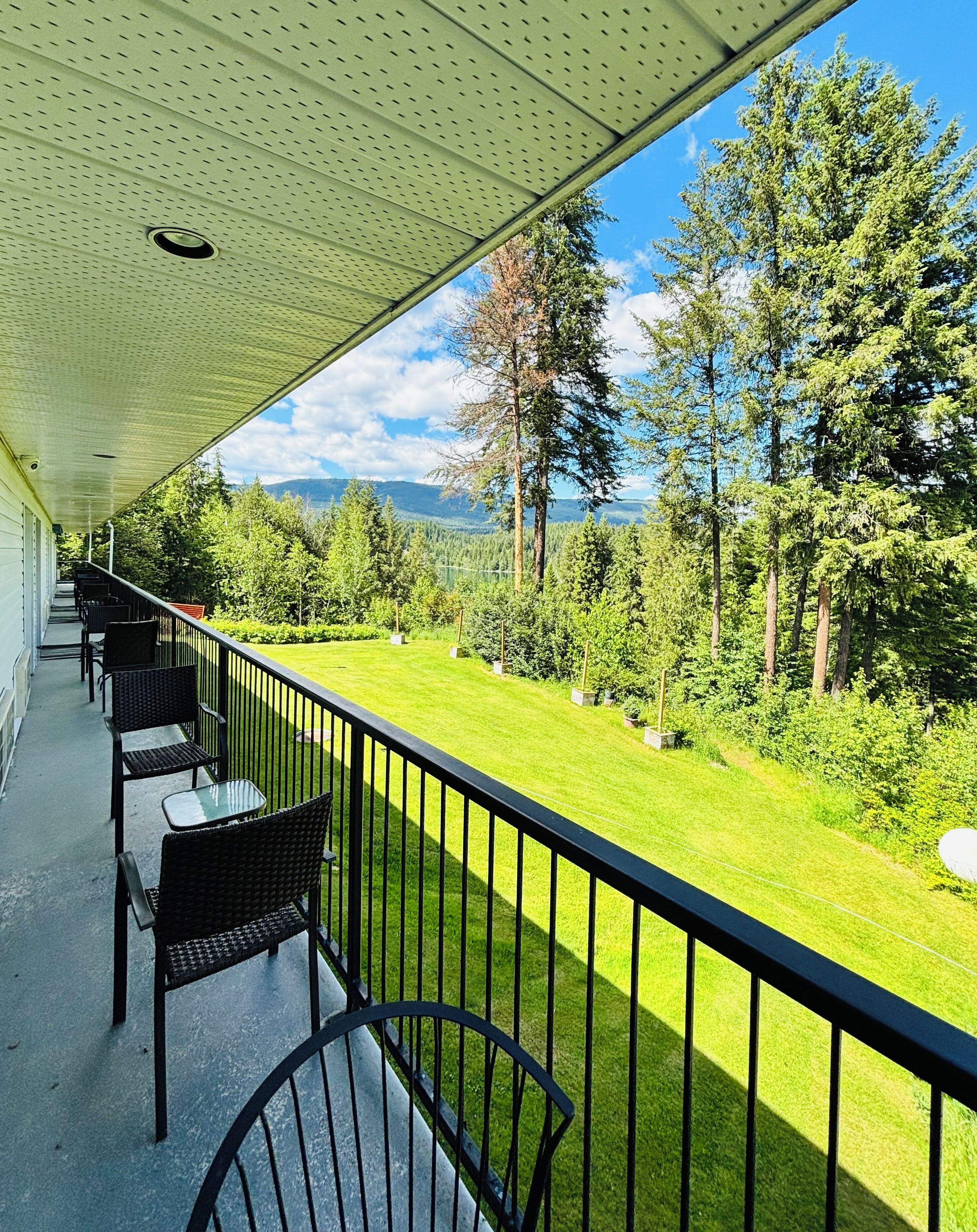 A balcony with outdoor seating, a view of a green landscape with trees, and a clear sky.