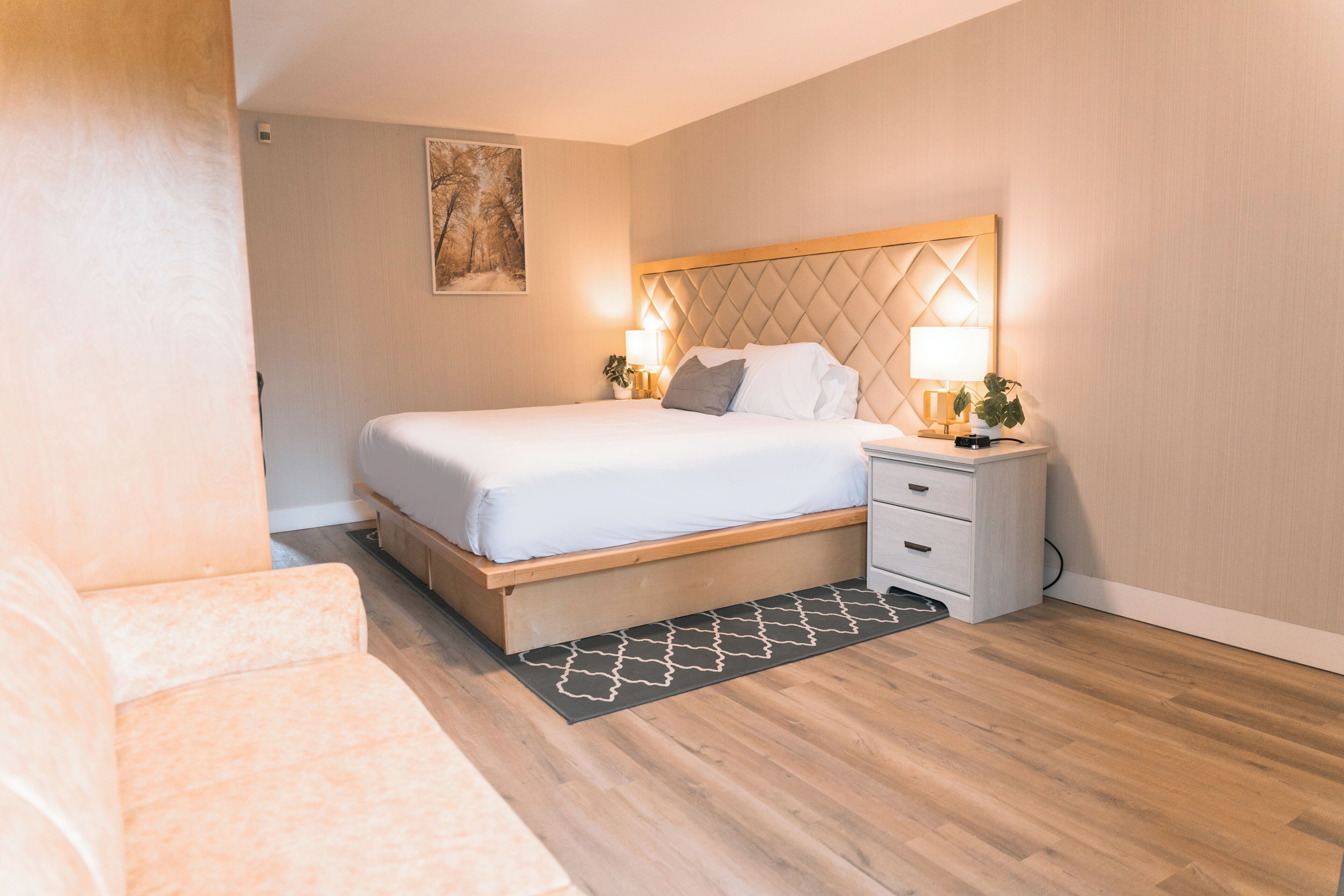 Quarto moderno com cabeceira de madeira, uma cama de casal, mesas de cabeceira com luminárias e uma pequena planta.