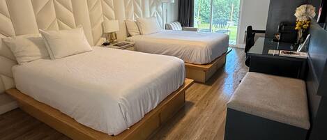A hotel room with two beds, a desk, a chair, and a view of the outdoors.