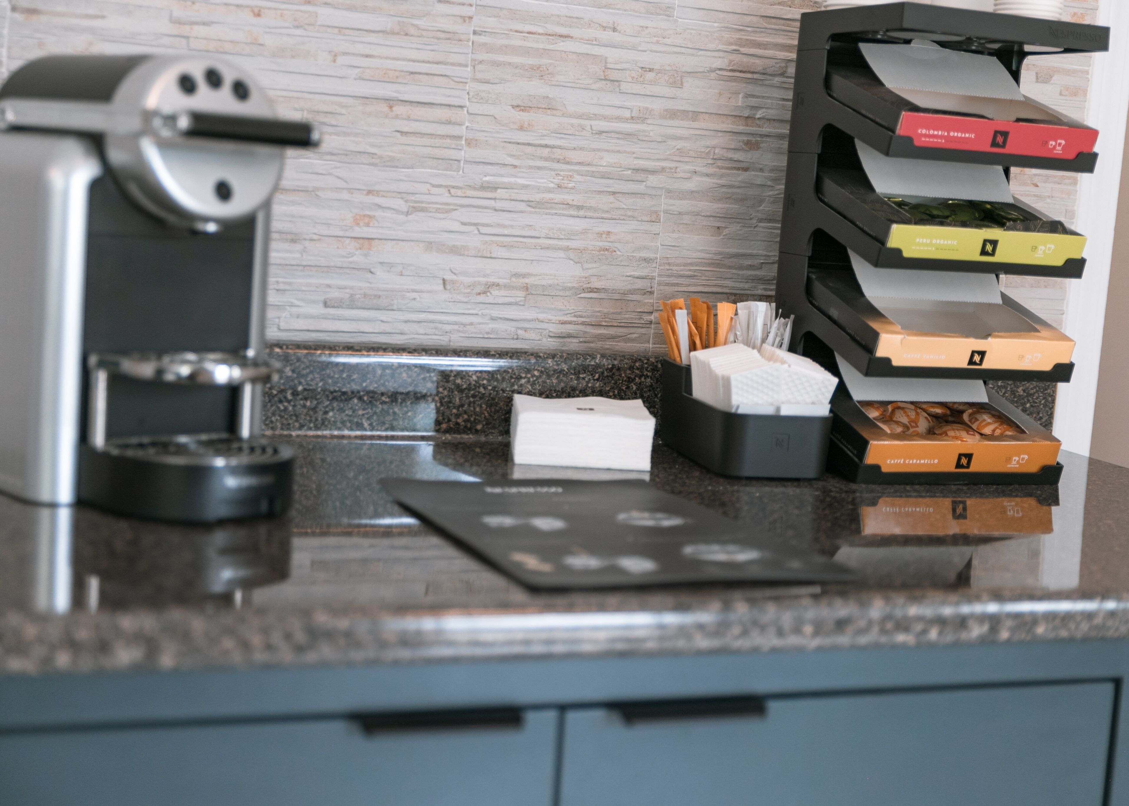 A coffee machine, a stack of coffee pods, and a napkin holder on a kitchen counter.