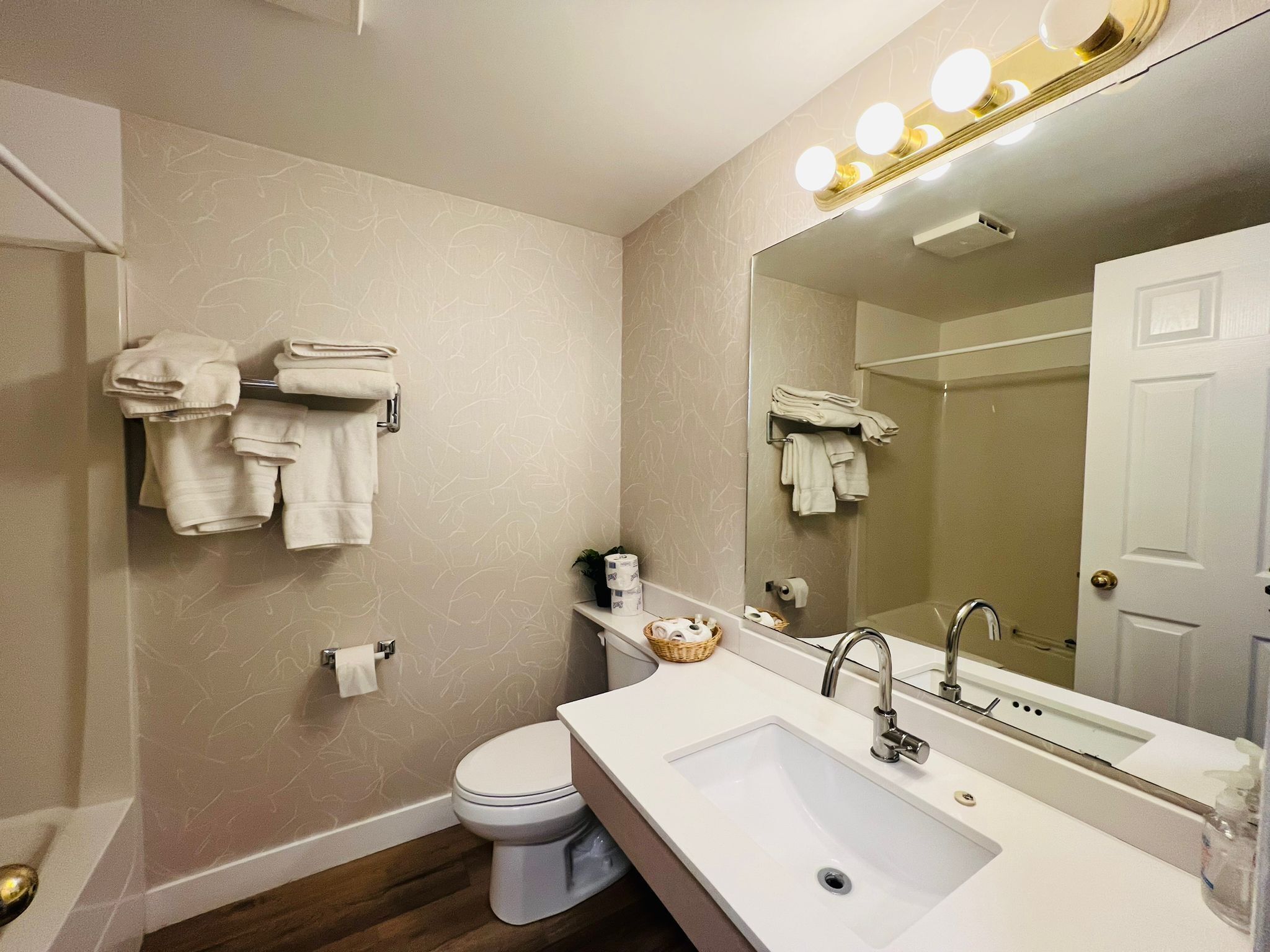 A modern bathroom with a white sink, a large mirror with lights, a toilet, and towels on a rack.
