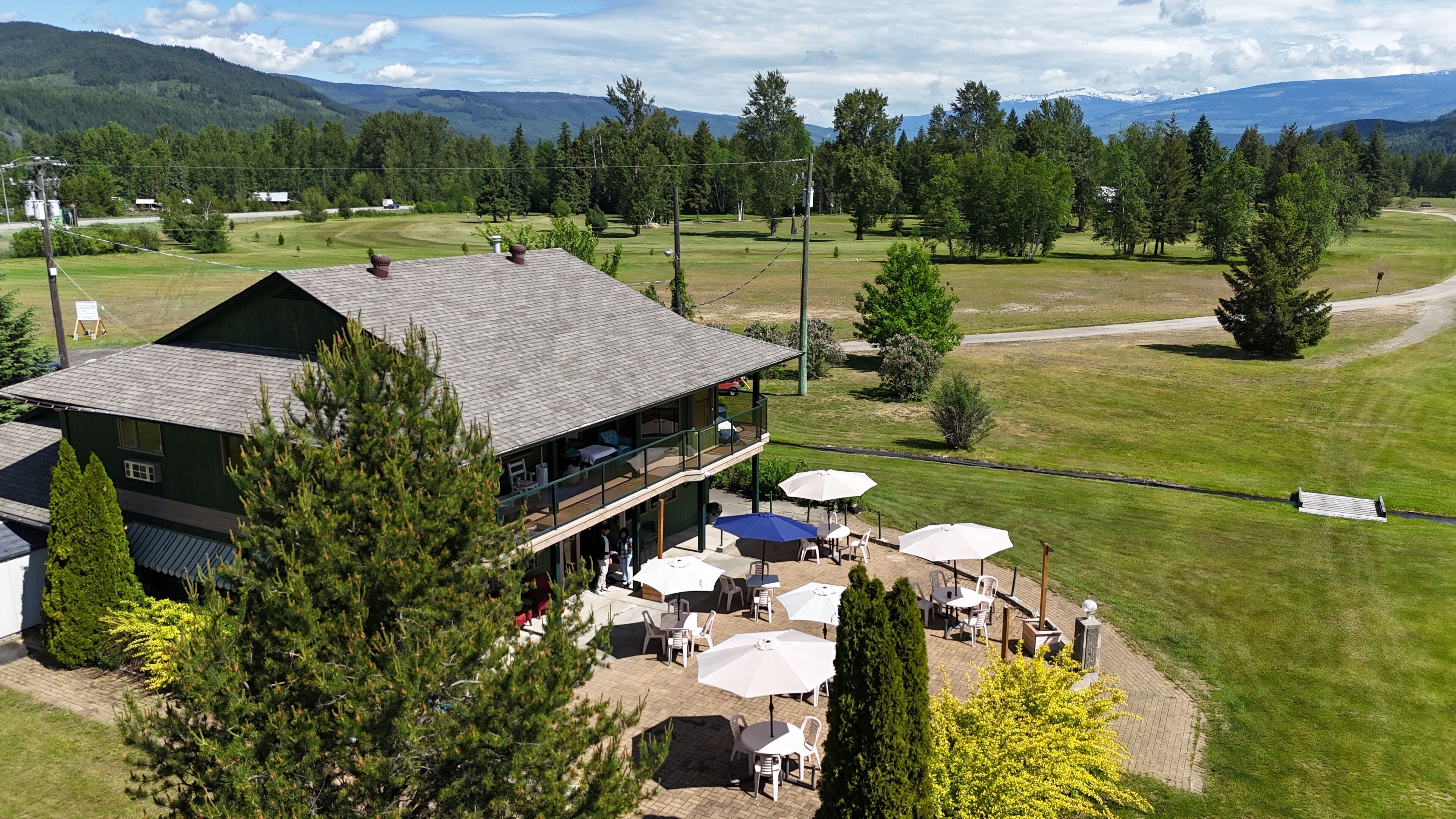 A two-story building with outdoor seating and a view of a golf course.