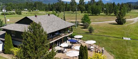 A two-story building with outdoor seating and a view of a golf course.
