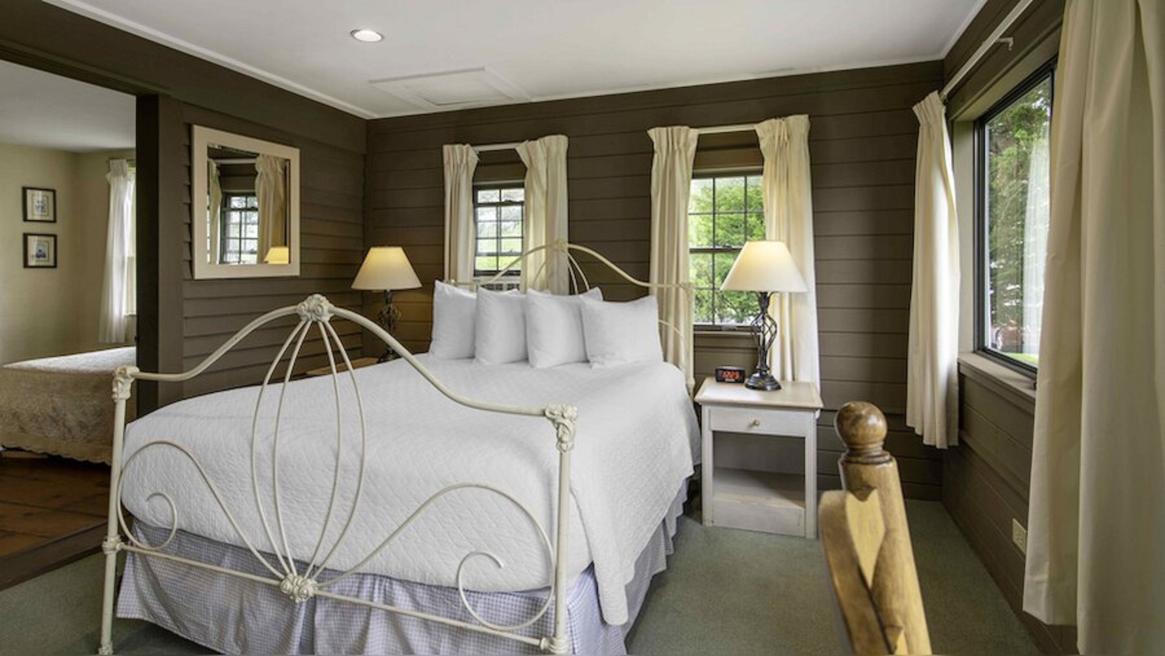 A bedroom with a four-poster bed, two bedside tables with lamps, a nightstand, and a window with curtains.