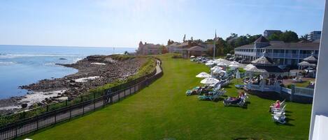 A coastal hotel with a grassy lawn, lounge chairs, umbrellas, and a view of the sea.