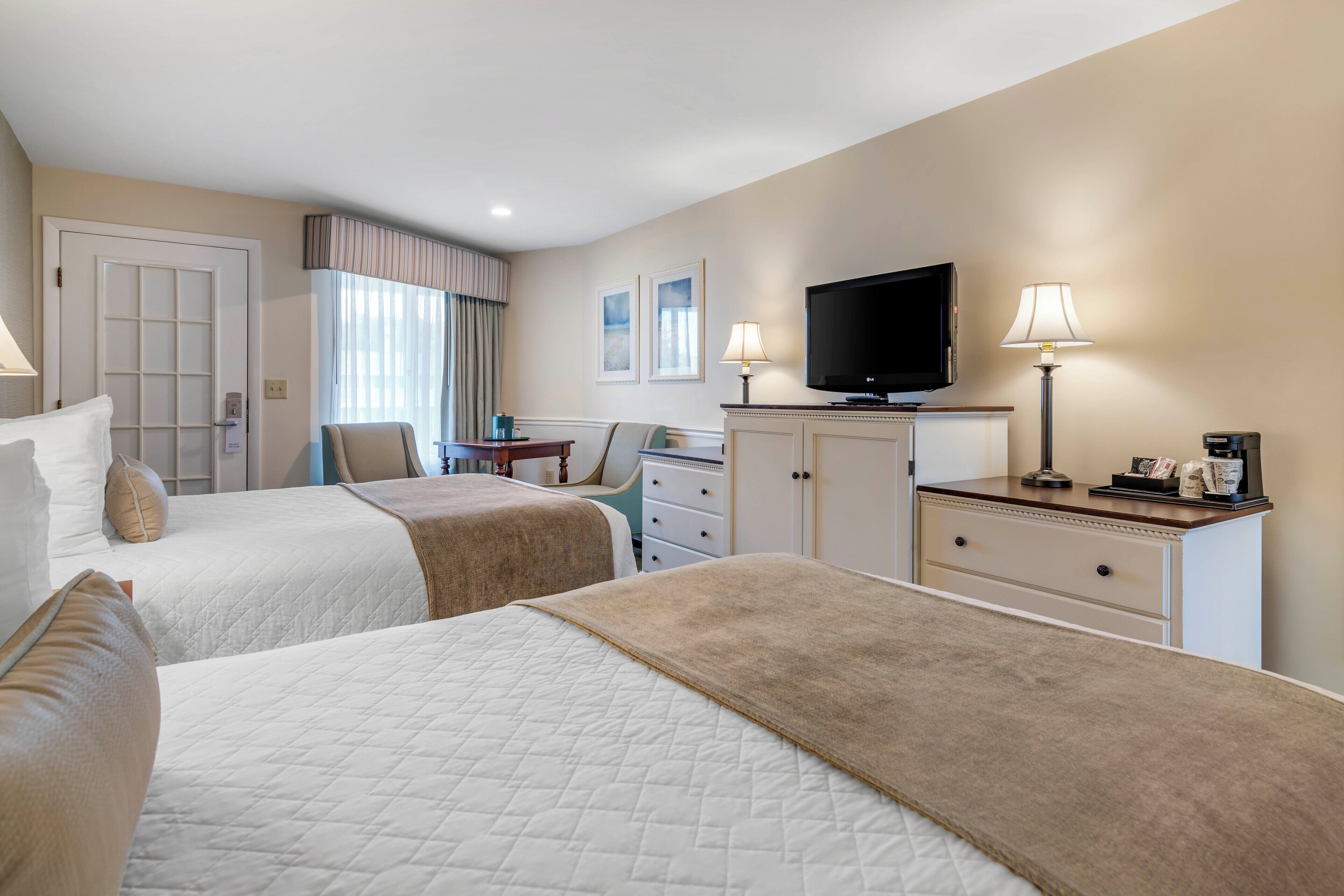A hotel room with two beds, a television, a desk, and a chair.