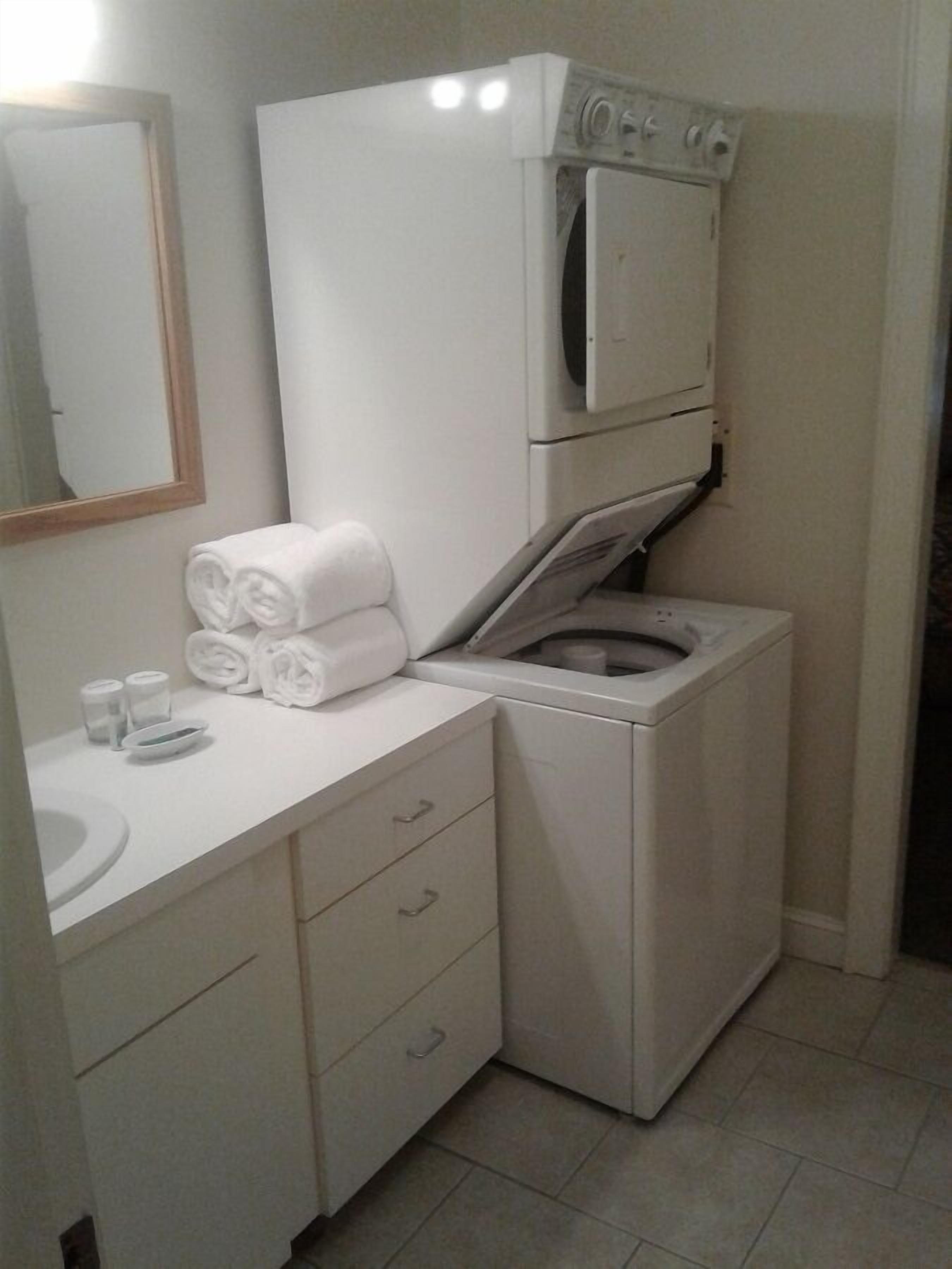 Casa de banho compacta e moderna, com máquina de lavar roupa e secadora integradas, uma pia e um espelho.