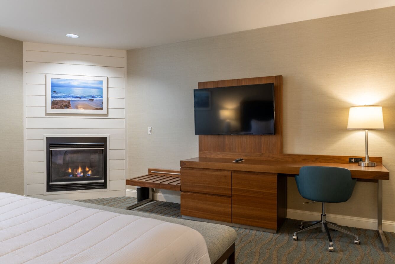 A hotel room with a bed, a fireplace, a desk with a TV, and a chair.