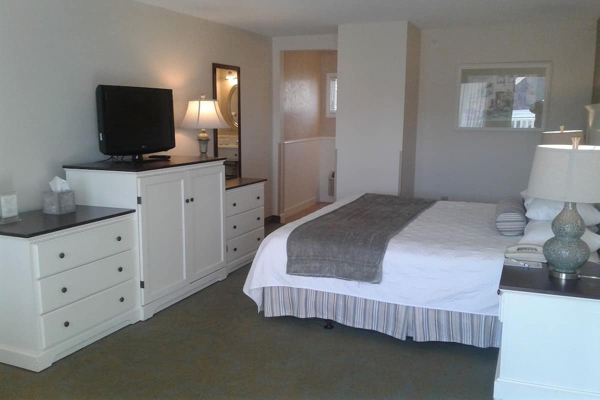 A hotel room with a bed, a television, a desk with a lamp, a dresser, and a mirror.