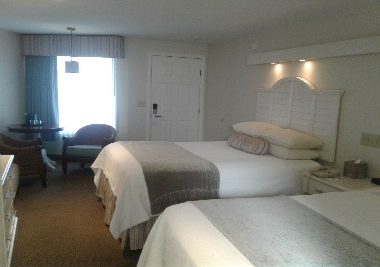 A hotel room with two beds, a desk, a chair, and a door.