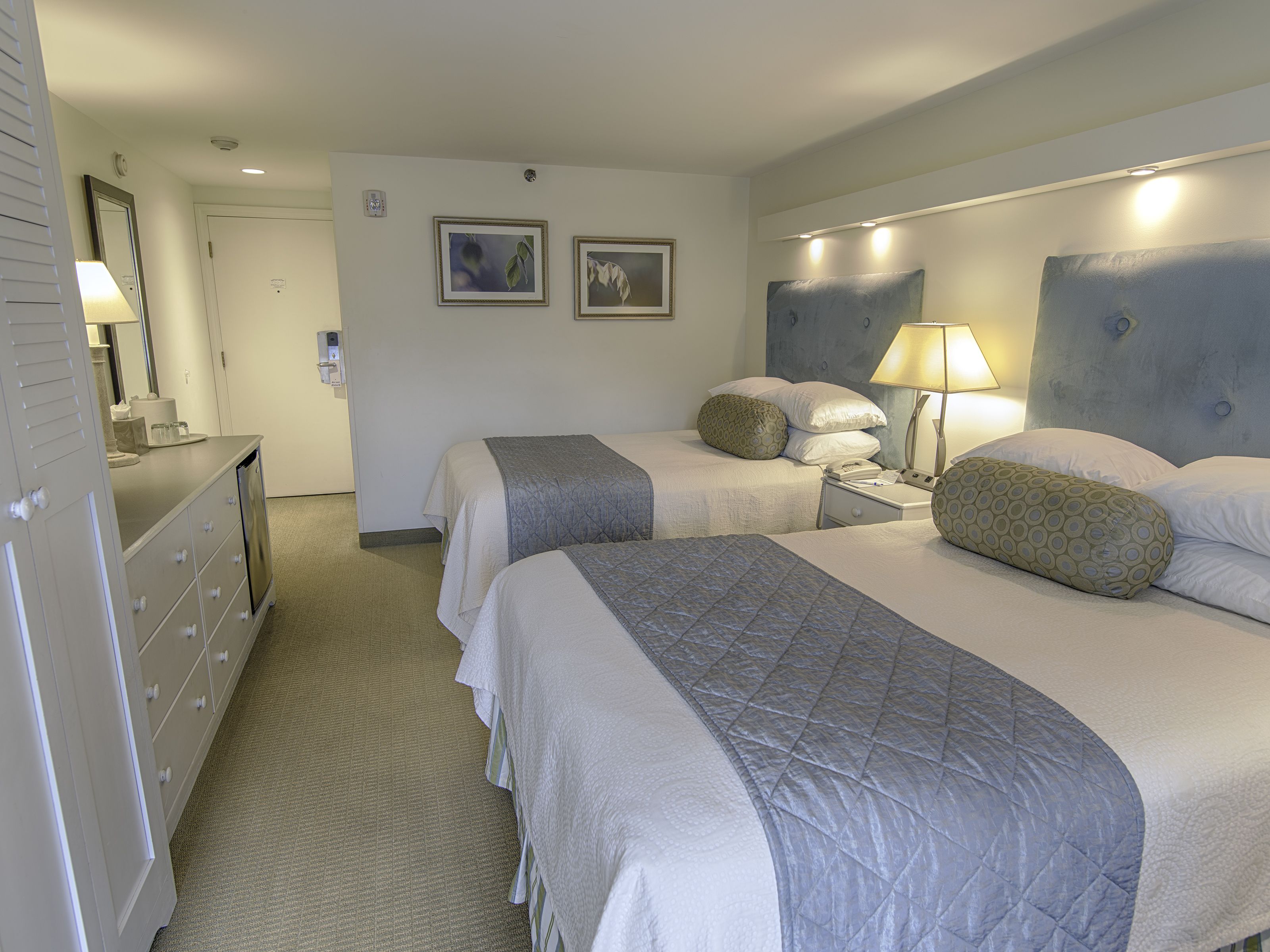 A hotel room with two beds, a dresser, a nightstand, and a lamp.