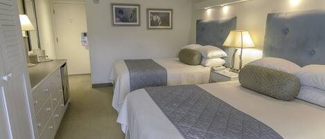 A hotel room with two beds, a dresser, a nightstand, and a lamp.