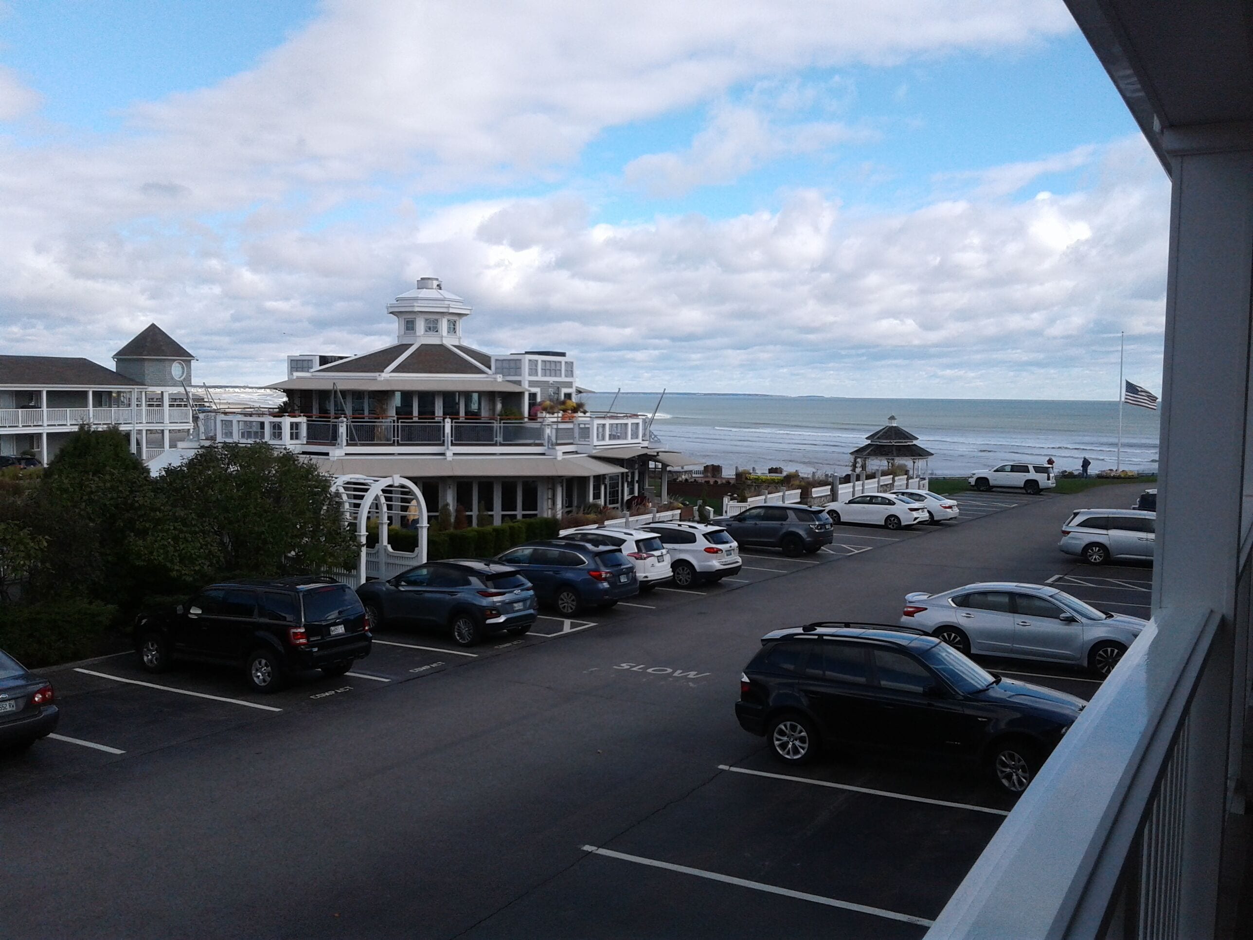 A coastal hotel with a parking lot, a gazebo, and a view of the ocean.