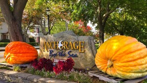 A sign with the text "Anchorage By the Sea" surrounded by large pumpkins and flowers. - Anchorage by the Sea (Ogunquit)