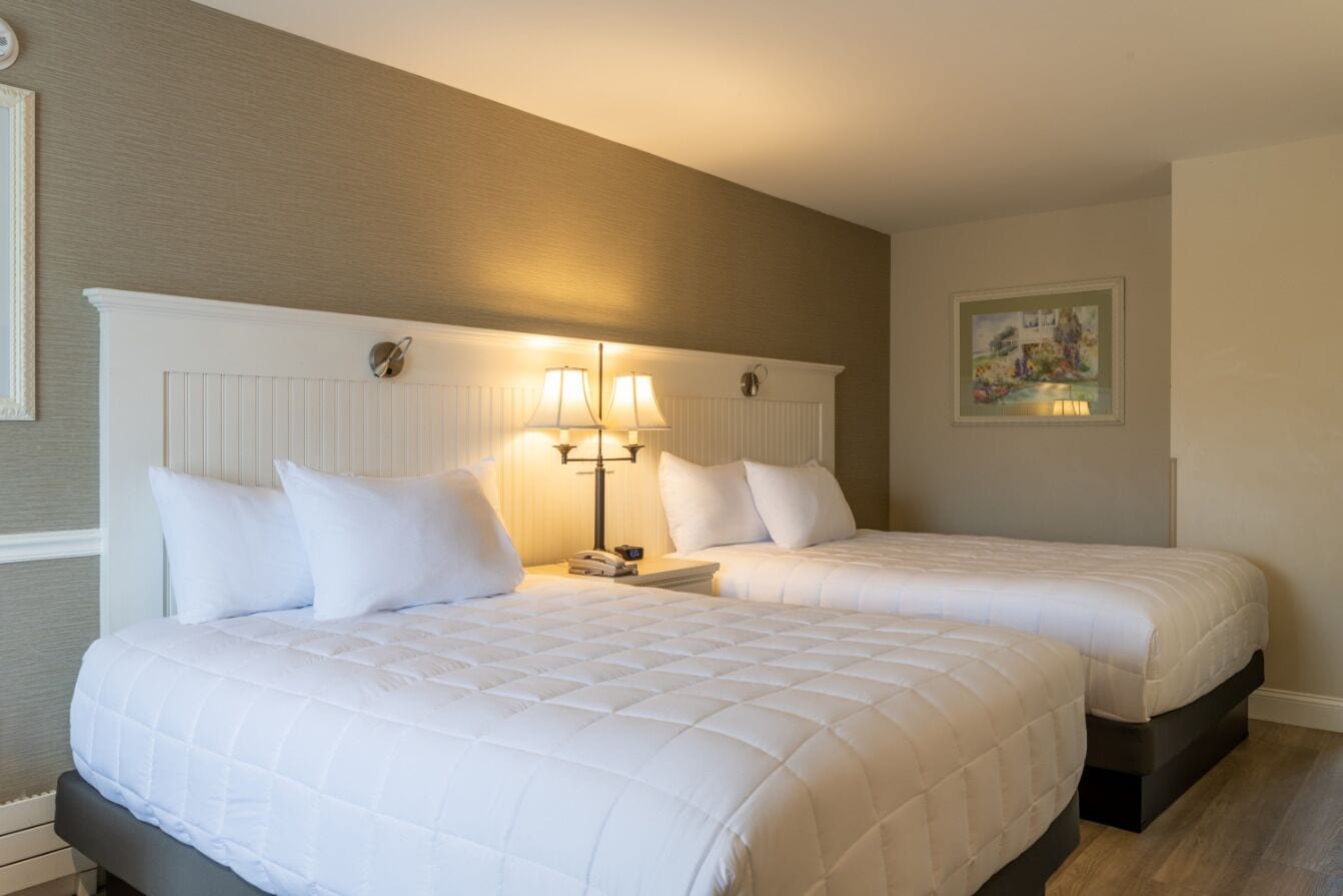 Une chambre d’hôtel avec deux lits, une table de chevet avec des lampes et un tableau encadré au mur.