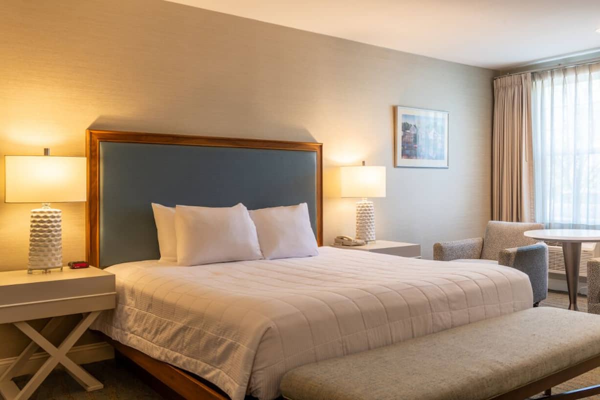 A hotel room with a large bed, two bedside tables with lamps, a small round table, and a chair.