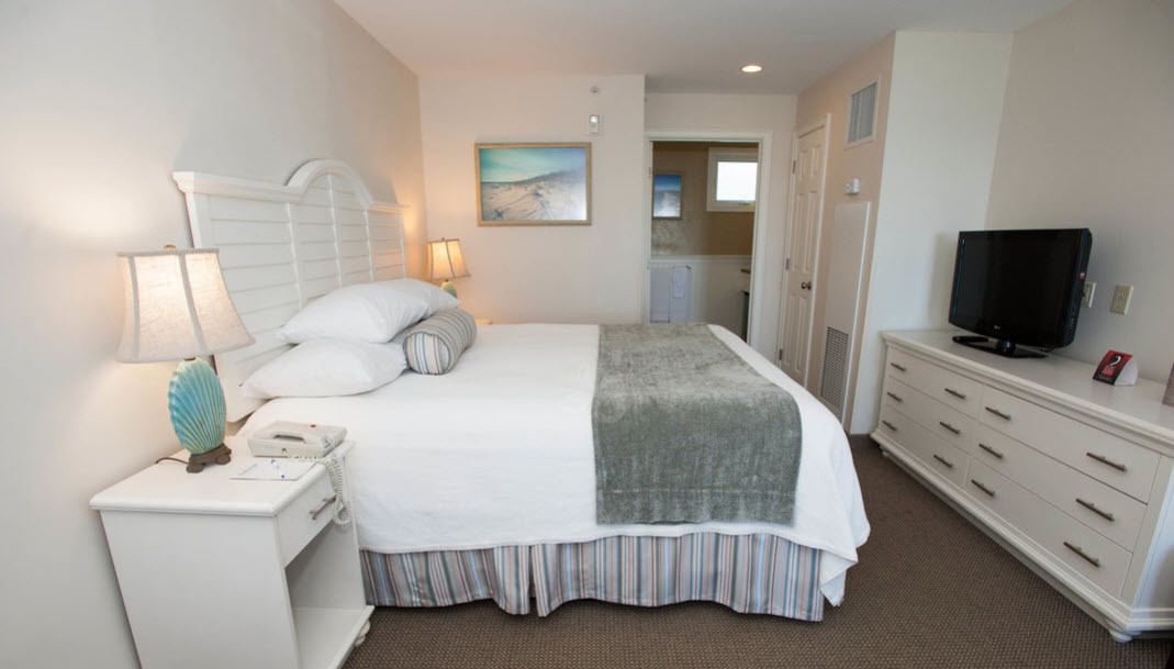 Habitación de hotel con cama, lámparas de noche, televisor, cómoda y un cuadro en la pared.