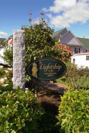 A sign for 'The Lightship at the Anchorage' with a lighthouse graphic, surrounded by greenery and a building in the background.