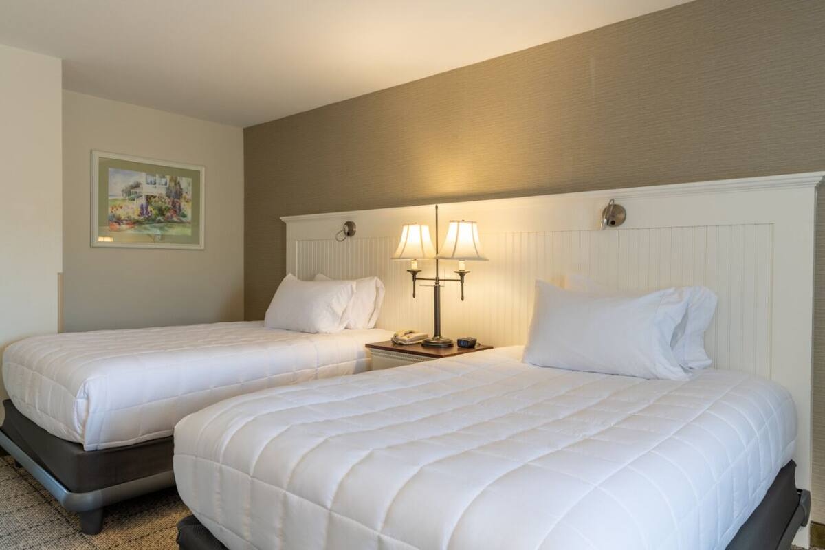 A hotel room with two beds, a nightstand with lamps, and a framed picture on the wall.