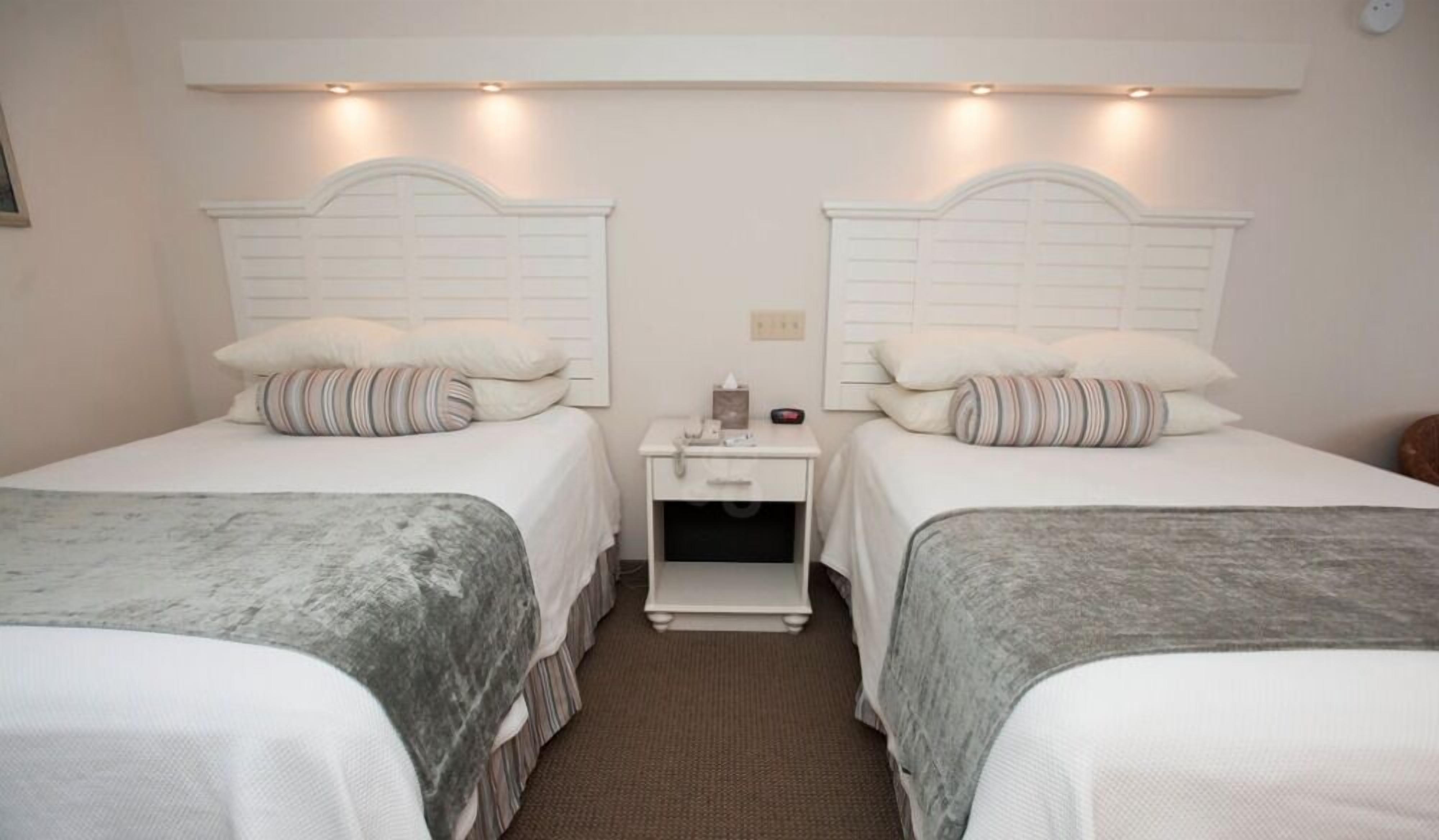 Una habitación de hotel con dos camas, cada una con cabecera, mesita de noche y lámpara.