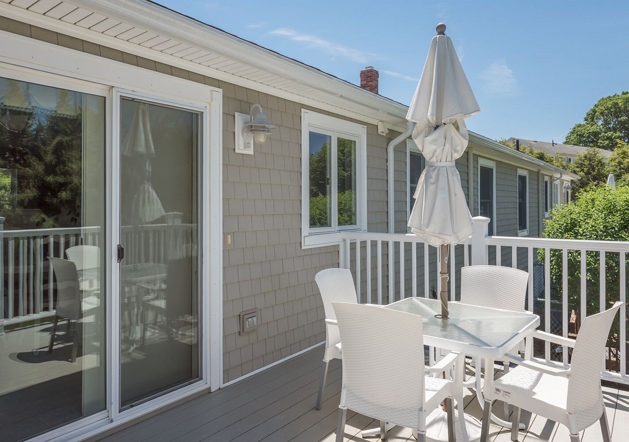 A covered patio with white furniture and a table, a sliding glass door, and a white railing.