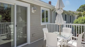A covered patio with white furniture and a table, a sliding glass door, and a white railing.