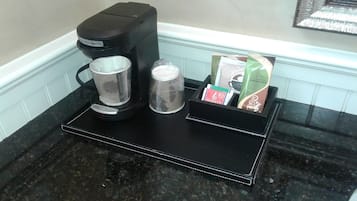 Una cafetera, un vaso y un soporte para cápsulas de café sobre una encimera negra.