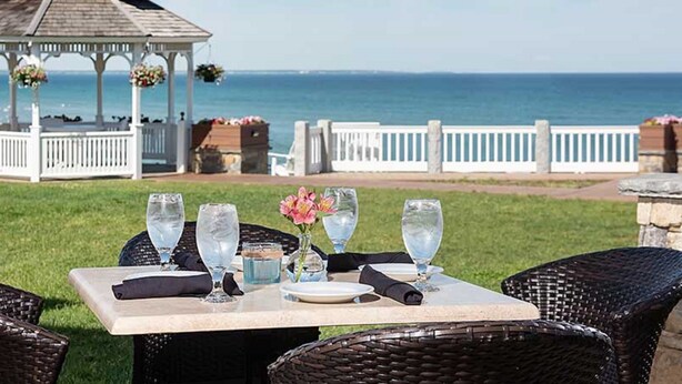 An outdoor dining area with a table set for two, overlooking the ocean. - Anchorage by the Sea (Ogunquit)