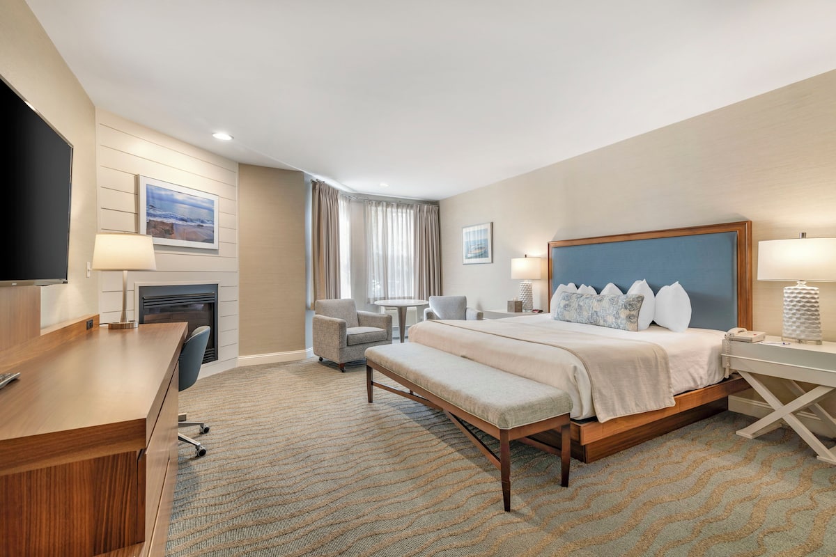A hotel room with a large bed, a desk, a chair, a TV, and a fireplace.