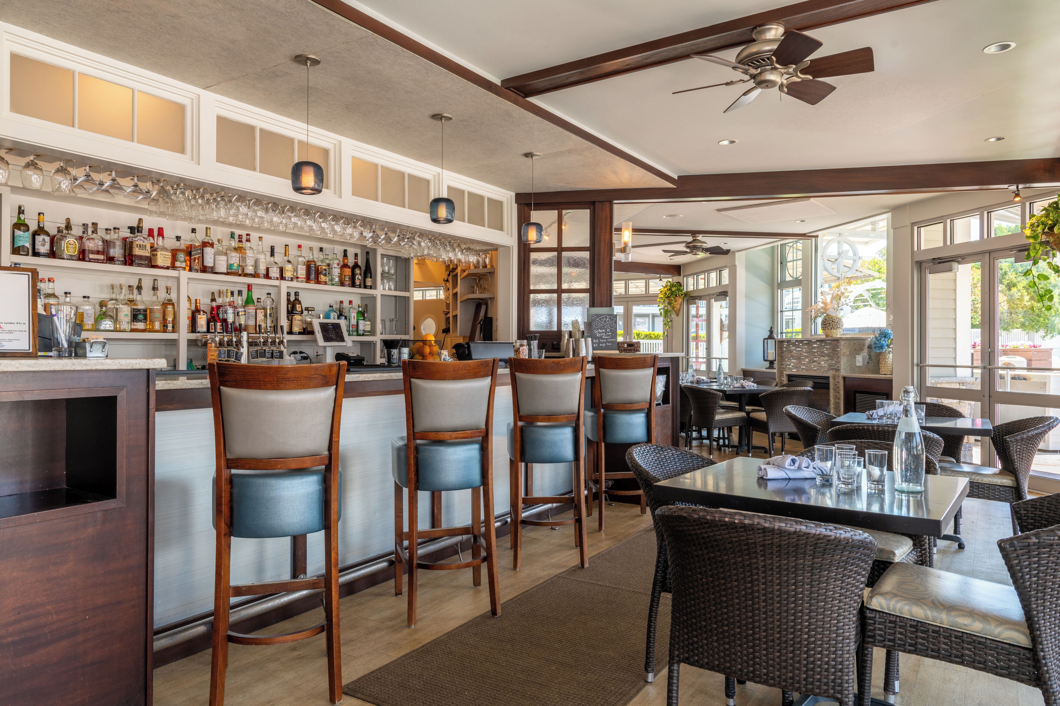 Een bar met verschillende krukken, een toonbank vol flessen en een zithoek met tafels en stoelen.
