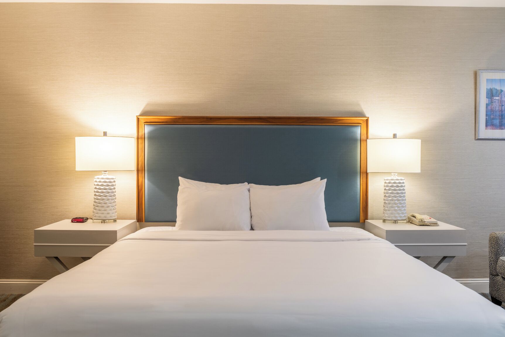 A hotel room with a large bed, two bedside tables, two lamps, and a framed picture on the wall.