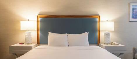 A hotel room with a large bed, two bedside tables, two lamps, and a framed picture on the wall.